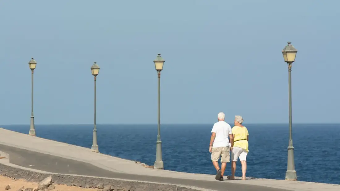 An older couple walking together along a seaside promenade